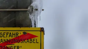Ein gelbes Warnschild mit Eiszapfen bei winterlichem Wetter und drohender Gefahr.