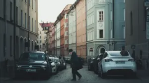 Ein Mann überquert eine belebte Straße in München zwischen geparkten Autos und historischen Gebäuden.
