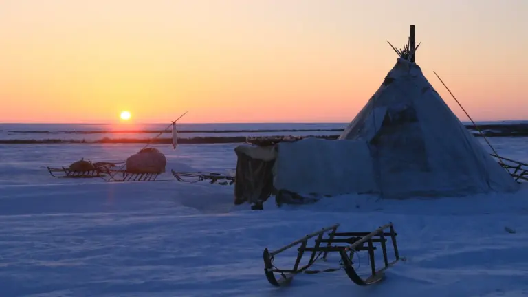 Ein traditionelles Tschum-Zelt im winterlichen Sibirien bei stimmungsvollem Sonnenuntergang am Horizont.