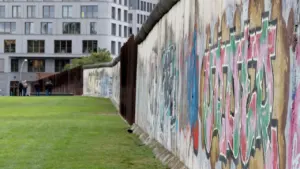 Blick entlang der bemalten Berliner Mauer mit grünem Park im Hintergrund.