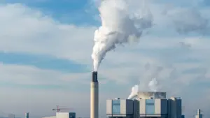 Ein großes Kraftwerk in Berlin stößt Dampf aus Schornsteinen in den bewölkten Himmel.
